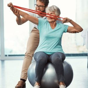 exercise professional helping elderly woman sitting on swiss ball with arm exercises